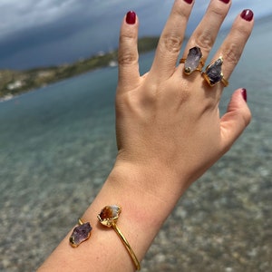 Puede incluir: Anillos de oro con piedras de amatista y citrino. Los anillos se llevan en una mano con esmalte de u&ntilde;as rojo. La mano tambi&eacute;n lleva una pulsera de oro con piedras de amatista y citrino.