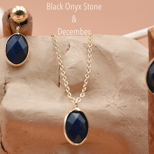May include: A gold necklace and earrings set with black onyx oval stones. The necklace has a delicate chain and the earrings are dangle style. Black Onyx Stone & December.