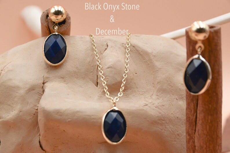 May include: A gold necklace and earrings set with black onyx oval stones. The necklace has a delicate chain and the earrings are dangle style. Black Onyx Stone & December.