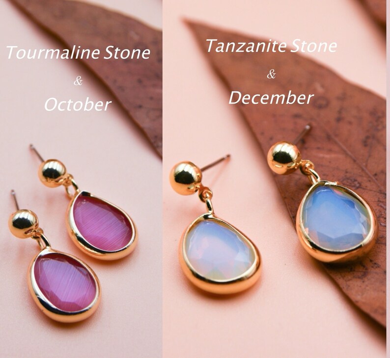May include: Two pairs of gold earrings with teardrop-shaped stones. The earrings on the left have pink stones and the text "Tourmaline Stone & October". The earrings on the right have light blue stones and the text "Tanzanite Stone & December".