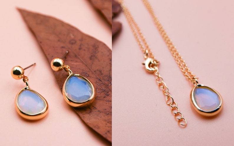 May include: A gold necklace and earrings set with a teardrop-shaped opal pendant. The opal is a light blue color with a white iridescent sheen.