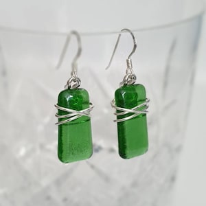 May include: A pair of silver dangle earrings with green glass rectangular charms wrapped in silver wire.