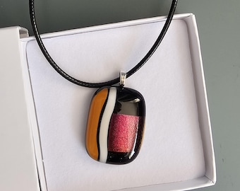 Colgante de vidrio dicroico en rojo y naranja sobre fondo negro.