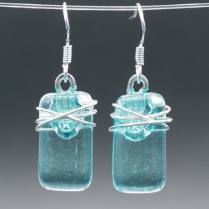 May include: A pair of silver wire wrapped earrings with light blue glass rectangular pendants.