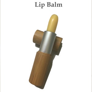 May include: A yellow lip balm in a bamboo tube with a silver cap. The tube is lying on its side with the cap off.