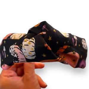 May include: A black fabric headband with a repeating pattern of orange, pink, and white pumpkins, stars, and purple mushrooms on a black background.