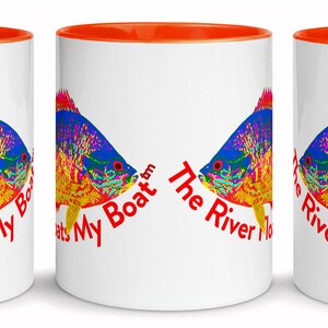 May include: White ceramic mug with an orange rim. The mug features a colourful fish illustration and the text "The River Floats My Boat" on the front.