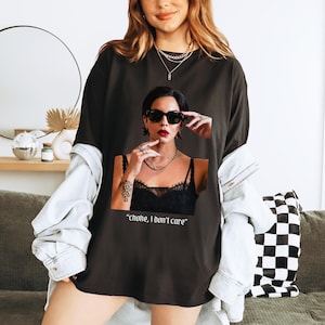 May include: Black t-shirt with a graphic print of a woman wearing sunglasses and a black lace top. The text "choke, I don't care" is printed below the image.