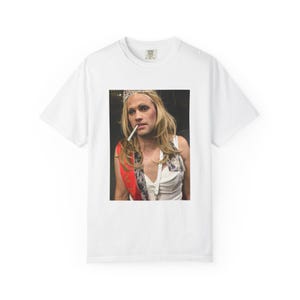 May include: White t-shirt featuring a photographic print of a person wearing a crown, sash, and makeup, holding a cigarette. The person is wearing a white top. The image is centered on the front of the shirt.