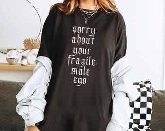 Op de afbeelding: Zwart oversized T-shirt met de tekst "sorry about your fragile male ego" in wit gedrukt.