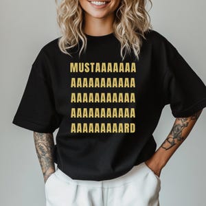 May include: Black t-shirt with gold text that reads "MUSTAAAAAAAAAAAA AAAAAAAAAAAAA AAAAAAAAAAAAA AAAAAAAAAAAAA AAAAAAAAAAARD"