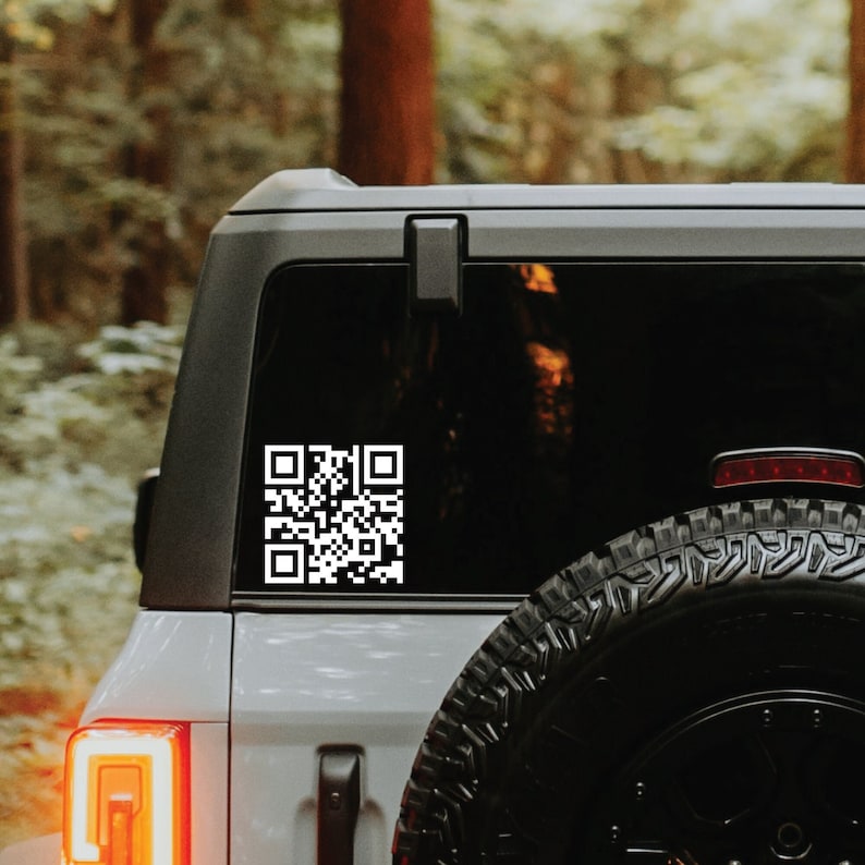 Op de afbeelding: Een witte QR-code sticker op de achterruit van een grijze SUV. De SUV heeft een zwarte band en een rood achterlicht.