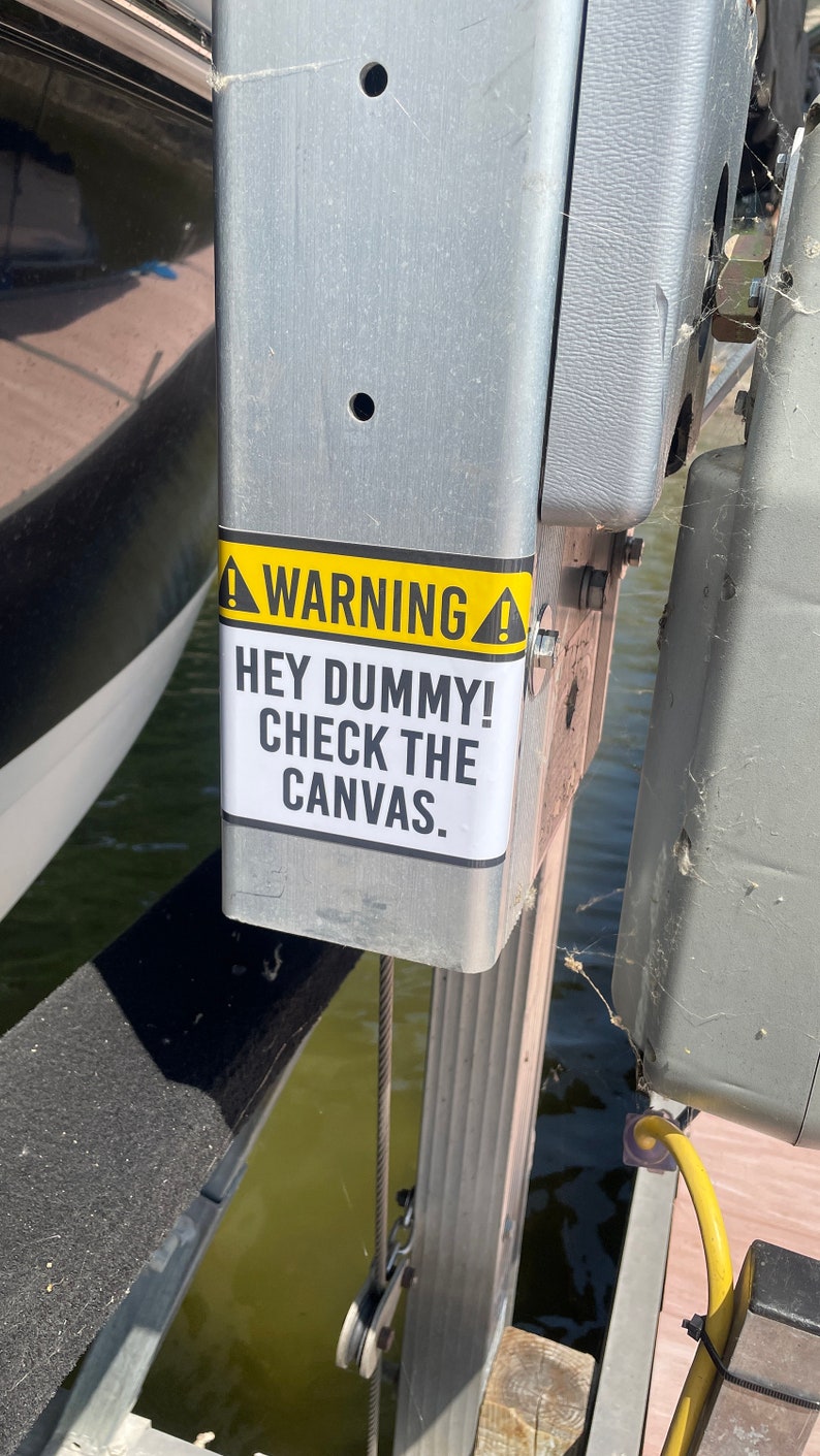 May include: A yellow and black warning sign with the text "WARNING! HEY DUMMY! CHECK THE CANVAS." attached to a metal post.