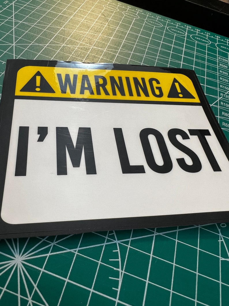 May include: A yellow and black warning sign with a white background and the text "WARNING! I'M LOST" in black.