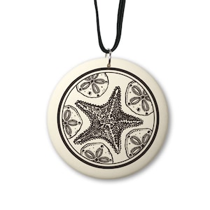 May include: A white ceramic pendant necklace with a black and white illustration of a starfish and four sand dollars inside a circle. The necklace has a black cord.