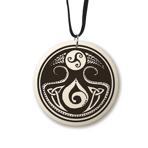 May include: A round ceramic pendant with a black and white design. The design features a Celtic knot, a triskelion, and a stylized teardrop. The pendant is on a black cord.