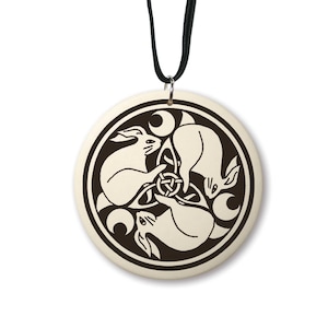 May include: A white ceramic pendant necklace with a black design of three rabbits in a circle with crescent moons. The pendant is on a black cord.