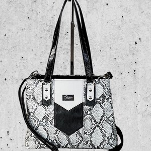 May include: A black and white snakeskin-patterned tote bag with black patent leather handles and accents. The bag features a white centre panel with a black chevron design and a small logo. Includes a detachable shoulder strap.