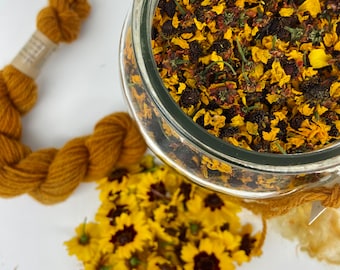 May include: A glass jar filled with dried yellow and brown flower petals. A skein of mustard-coloured yarn and a bundle of sunflowers are next to the jar. The items are arranged on a white surface.