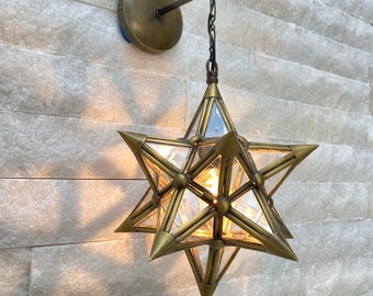 May include: A brass star-shaped pendant light fixture with clear glass panels. The light is hanging from a chain and is attached to a wall mount.