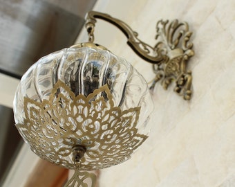 May include: A clear glass globe pendant light fixture with a decorative brass frame and a brass wall mount. The globe has a ribbed texture and a delicate, intricate pattern.
