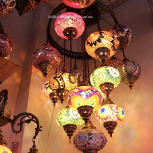 Puede incluir: Una l&aacute;mpara de ara&ntilde;a de varios niveles con globos redondos de vidrio de mosaico de colores. Los globos est&aacute;n suspendidos de un marco de metal con cadenas. La l&aacute;mpara de ara&ntilde;a est&aacute; encendida y proyecta un brillo c&aacute;lido.