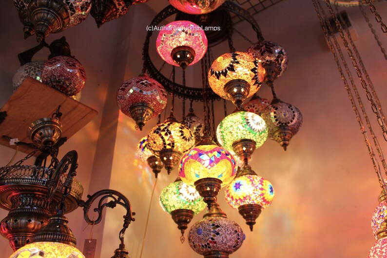Puede incluir: Una l&aacute;mpara de ara&ntilde;a de varios niveles con globos redondos de vidrio de mosaico de colores. Los globos est&aacute;n suspendidos de un marco de metal con cadenas. La l&aacute;mpara de ara&ntilde;a est&aacute; encendida y proyecta un brillo c&aacute;lido.
