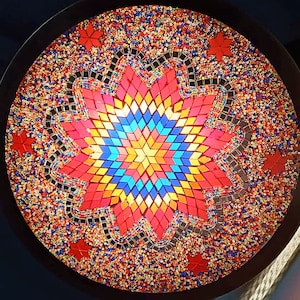 May include: A round, mosaic-style ceiling light fixture with a large, multi-colored star in the center. The star is made of small, square tiles in shades of red, orange, yellow, blue, and green. The surrounding background is a mix of red, orange, yellow, and gold tiles.