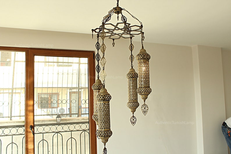 Puede incluir: L&aacute;mpara de ara&ntilde;a ornamentada de estilo antiguo con acabado en bronce. La l&aacute;mpara presenta m&uacute;ltiples l&aacute;mparas colgantes con intrincados dise&ntilde;os calados y paneles de vidrio transparente. Las l&aacute;mparas est&aacute;n suspendidas de un marco de metal decorativo.