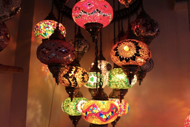 Puede incluir: Una l&aacute;mpara de ara&ntilde;a de varios niveles con globos de vidrio redondos y coloridos. Los globos est&aacute;n hechos de mosaicos de azulejos en tonos de rojo, naranja, amarillo, verde y azul. La l&aacute;mpara de ara&ntilde;a est&aacute; colgada del techo y est&aacute; iluminada, proyectando un brillo c&aacute;lido.
