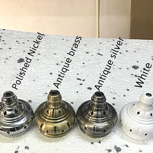 May include: Close-up of seven different colored metal lamp finials. The finials are arranged in a row from left to right: polished copper, polished nickel, antique brass, antique silver, white, and black.