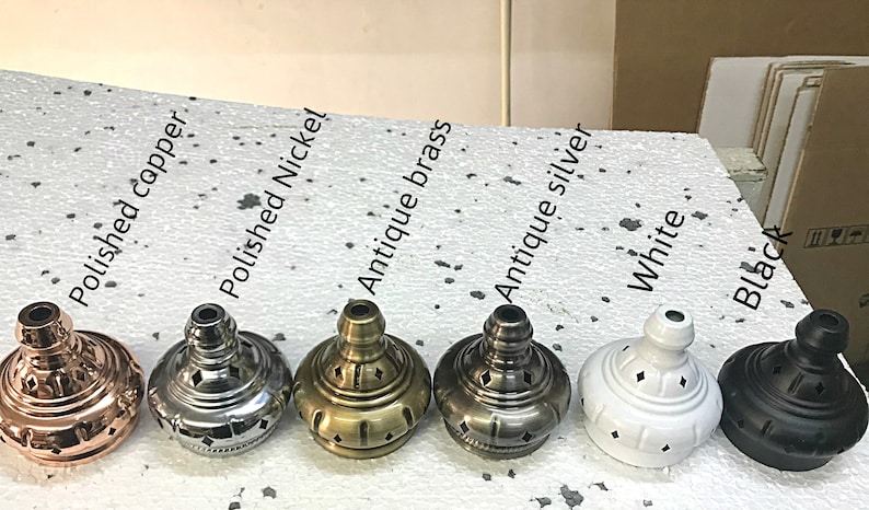May include: Close-up of seven different colored metal lamp finials. The finials are arranged in a row from left to right: polished copper, polished nickel, antique brass, antique silver, white, and black.