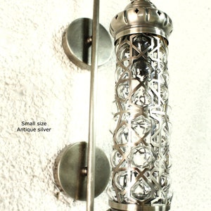 May include: Antique silver wall sconce with a geometric patterned glass shade. The sconce has a simple, modern design and is perfect for adding a touch of elegance to any room.