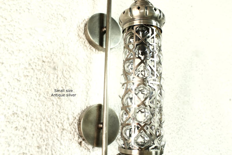 May include: Antique silver wall sconce with a geometric patterned glass shade. The sconce has a simple, modern design and is perfect for adding a touch of elegance to any room.