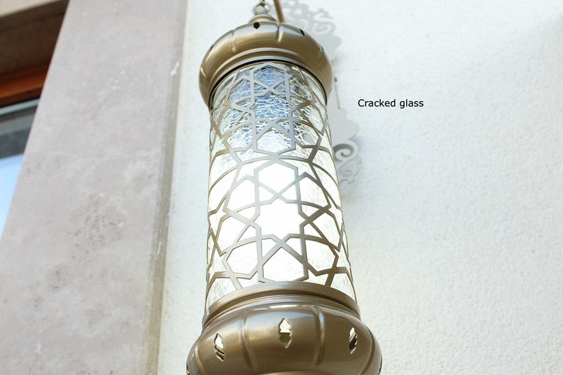 May include: A gold-toned metal lantern with a clear glass panel featuring a geometric pattern. The glass panel has a cracked appearance.
