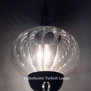 May include: A clear glass Turkish pendant lamp with a black metal frame and a decorative design. The lamp is lit and the light shines through the glass.