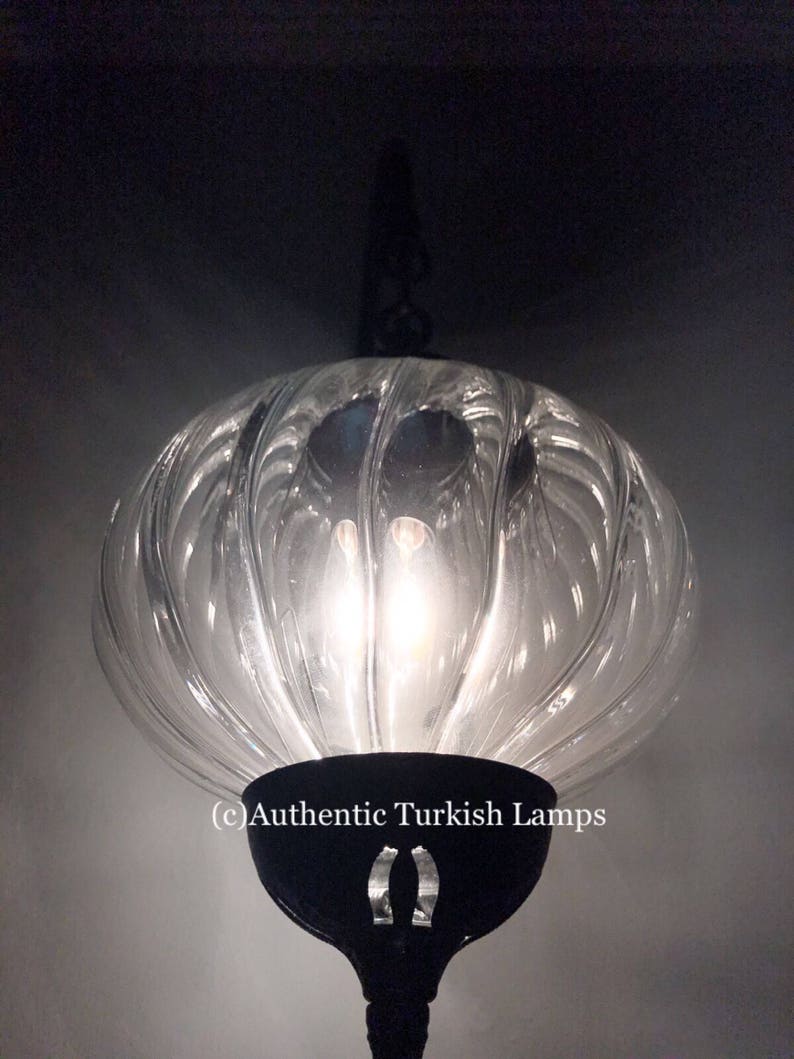 May include: A clear glass Turkish pendant lamp with a black metal frame and a decorative design. The lamp is lit and the light shines through the glass.