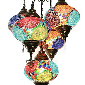 Op de afbeelding: Een veelkleurige mozaïekglazen kroonluchter met vijf ronde bollen. De bollen zijn gemaakt van kleine stukjes glas in tinten blauw, groen, rood, geel en oranje. De kroonluchter heeft een rustieke bronzen afwerking.