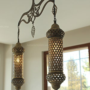 May include: Two ornate, antique-style hanging lamps with a warm glow. The lamps have intricate metalwork and a cylindrical shape, suspended from a decorative metal bar. These lamps are perfect for adding a touch of elegance to any room.