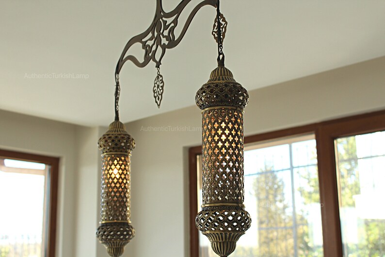May include: Two ornate, antique-style hanging lamps with a warm glow. The lamps have intricate metalwork and a cylindrical shape, suspended from a decorative metal bar. These lamps are perfect for adding a touch of elegance to any room.
