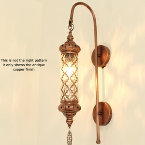 May include: An antique copper wall sconce with a cylindrical glass shade featuring a geometric pattern. The sconce has a curved arm and a round base.