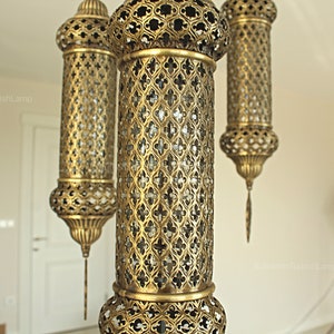 Puede incluir: L&aacute;mparas colgantes doradas ornamentadas con intrincados dise&ntilde;os de metal calado. Las l&aacute;mparas tienen forma cil&iacute;ndrica con partes superiores e inferiores decorativas y cuelgan del techo. Un accesorio de iluminaci&oacute;n decorativo.