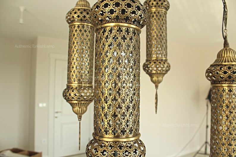 Puede incluir: L&aacute;mparas colgantes doradas ornamentadas con intrincados dise&ntilde;os de metal calado. Las l&aacute;mparas tienen forma cil&iacute;ndrica con partes superiores e inferiores decorativas y cuelgan del techo. Un accesorio de iluminaci&oacute;n decorativo.