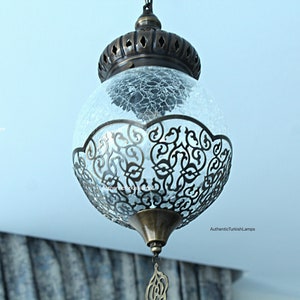 May include: A round, clear glass pendant light with a decorative metal frame. The glass has a crackled finish and the frame has a filigree design.