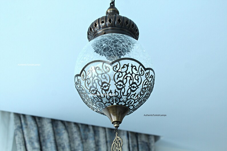 May include: A round, clear glass pendant light with a decorative metal frame. The glass has a crackled finish and the frame has a filigree design.