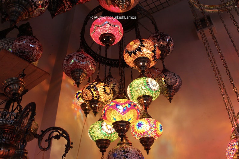 Puede incluir: Una l&aacute;mpara de ara&ntilde;a de varios niveles con globos de vidrio de mosaico de colores. Los globos est&aacute;n suspendidos de un marco de metal con cadenas. La l&aacute;mpara de ara&ntilde;a est&aacute; encendida y proyecta un brillo c&aacute;lido.