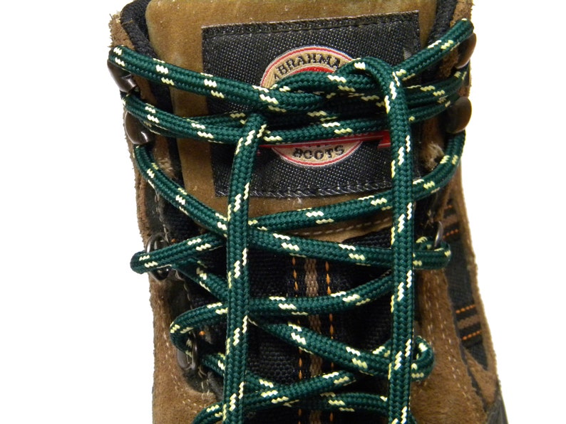 May include: Close-up of brown leather hiking boots with green and white laces. The boots have a black label with the text "ABRAHAM BOOTS".