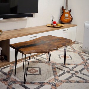 May include: A live edge wood coffee table with a black epoxy river and hairpin legs. The table is sitting on a patterned tile floor in a living room setting.