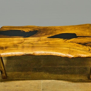 Può includere: Tavolino da caffè in legno fatto a mano con design a bordo vivo. Il tavolo presenta una finitura naturale con venature del legno e intarsi in resina epossidica scura. Le gambe in legno angolate creano un'estetica unica e rustica.