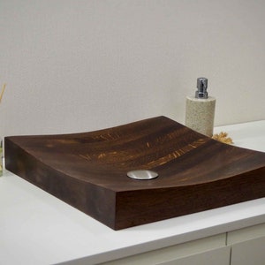 Peut inclure: Un &eacute;vier en bois brun fonc&eacute; avec un design incurv&eacute; et un drain argent&eacute;. L'&eacute;vier est pos&eacute; sur un comptoir blanc.